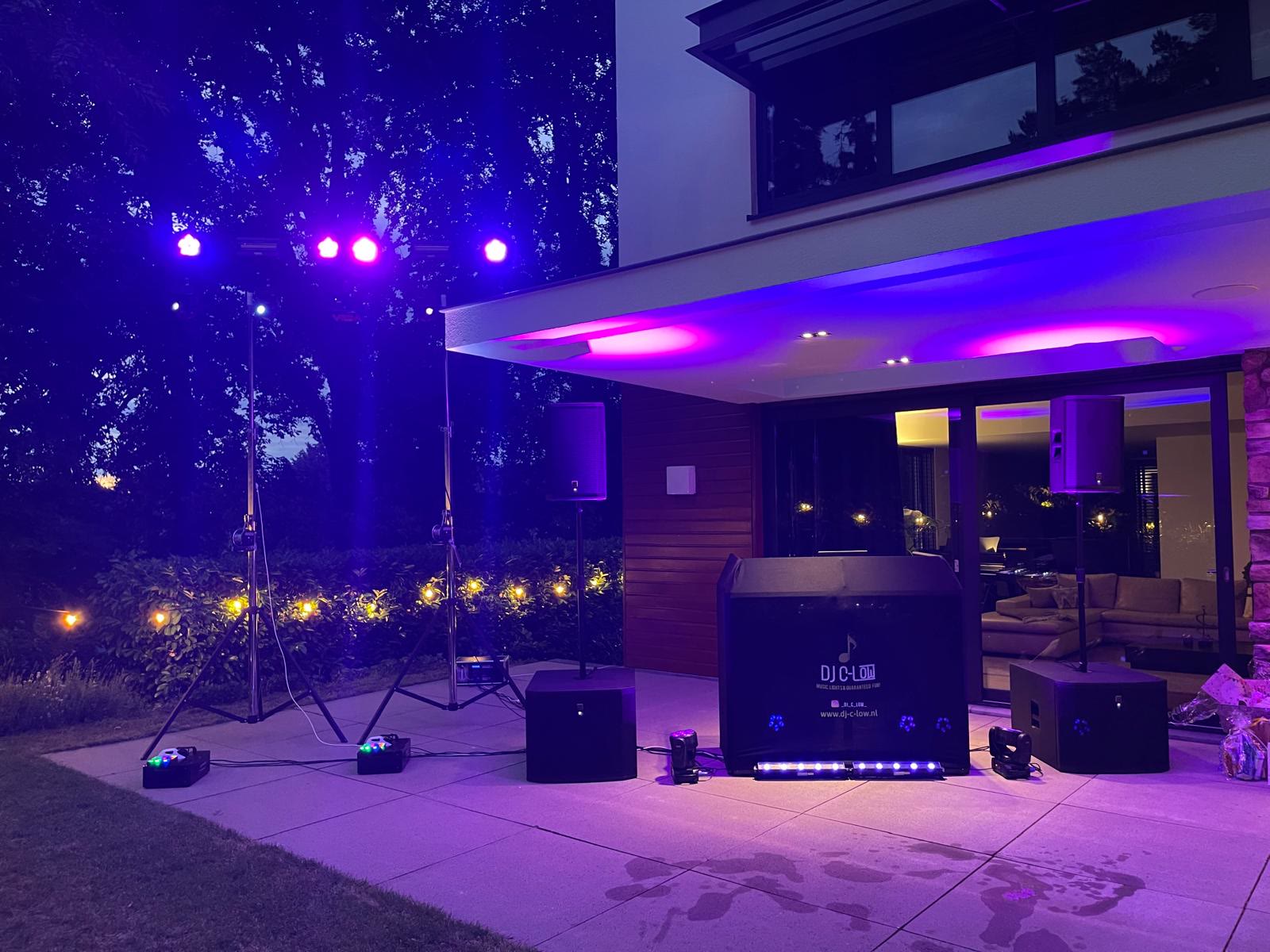 Speakers, subwoofers en een DJ-booth in paars licht op een terras